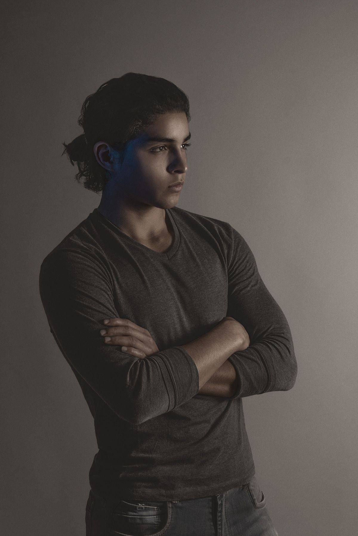 A young man in profile in low editorial light, arms folded